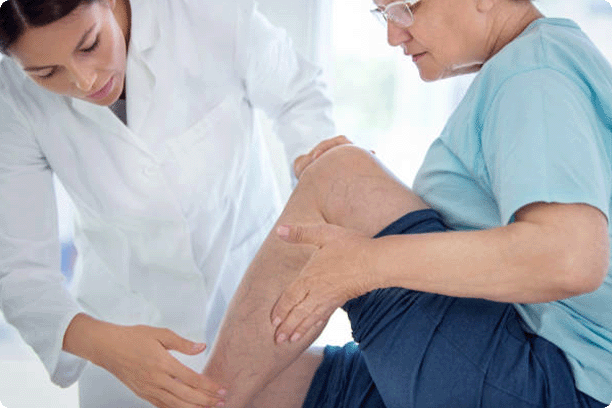 female doctor massaging legs and calves of a senior female patient with visible varicose veins